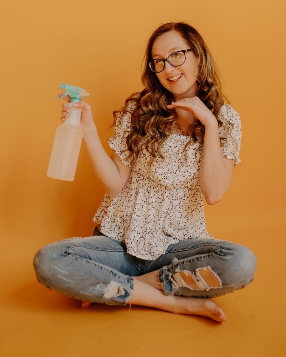 Taylor Hutson, owner of Clean with Grace, smiling with a spray bottle